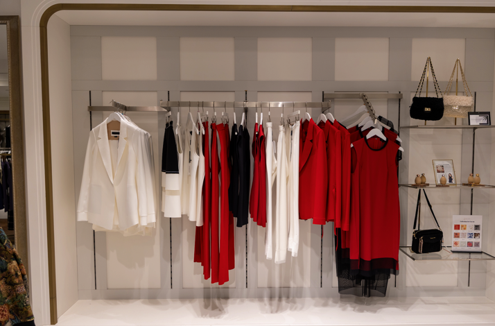 Retail display wall featuring structured red, white, and black women's clothing alongside designer handbags on shelves.