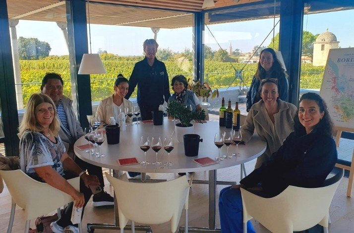 A group of tourists sitting at a round table prepared for wine degustation at one of the Bordeaux vineyards.