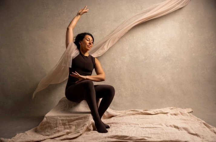 Breathwork teacher Sophia Manassei in black sitting with a hand up position during transformative session of The Class. 