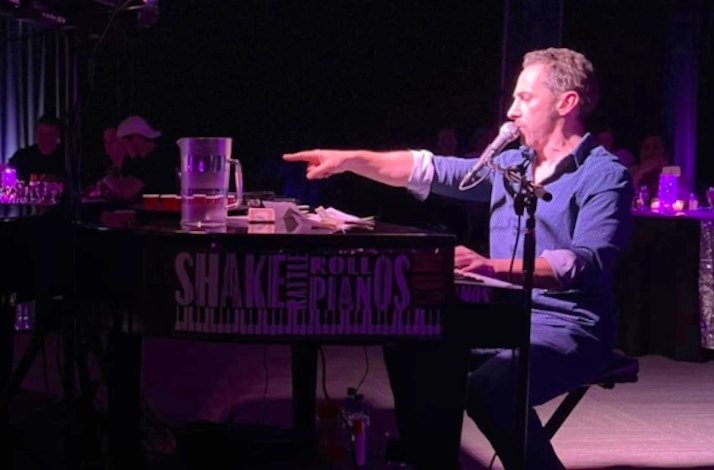 An artist sitting at the piano pointing with his hand.