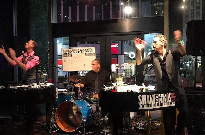 Two of the top piano entertainers in NYC playing songs on stage joined by a drummer.
