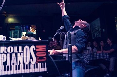 An artist sitting at the piano throwing his hand up.