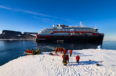 A group of persons doing an expedition to Antartica with MS Roald Amundsen ship at the background.