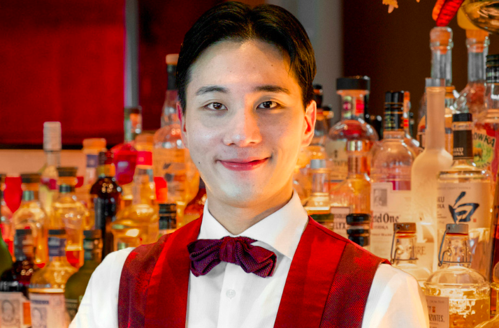 Another bartender in a red vest and bow tie, also in front of a bar with bottles.