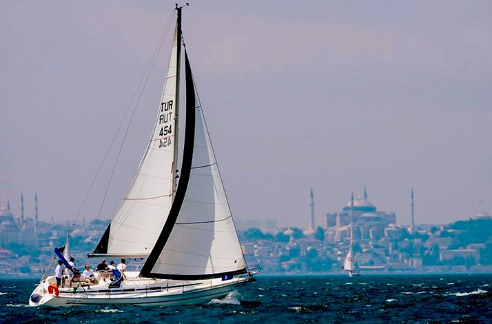 A white sailboat sailing on the Bosphorus in Istanbul, with the historic city skyline featuring Hagia Sophia and mosque minarets in the background.