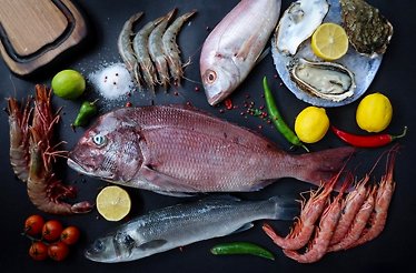 A colorful seafood spread with fish, shrimp, oysters, and lemons on a black surface.