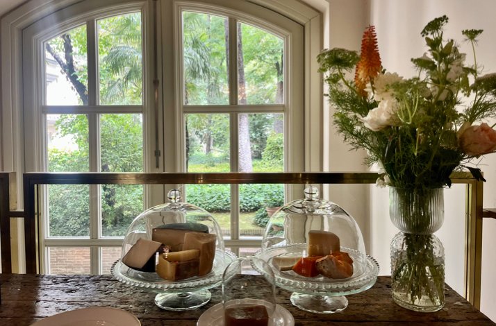  Cheese selections under glass cloches on a marble table by a large window, with a vase of flowers, at Club Matador.