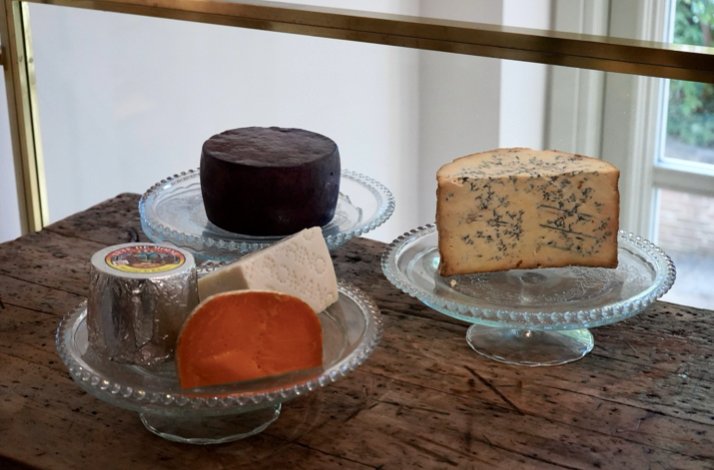 Assorted cheeses at Club Matador, displayed on glass stands, including a wedge of blue cheese, on a rustic table.