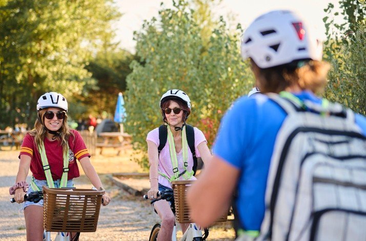 Two women and a man on the bicycles wearing sunglasses and helmets.