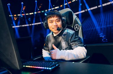 Smiling player giving a thumbs-up at a League of Legends Worlds pro stage setup, wearing a team jersey and gaming headset.