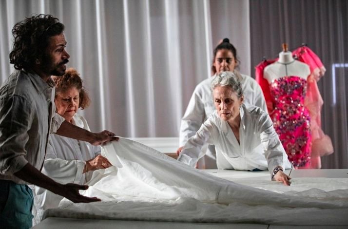 Performers examine a white wedding dress together on stage.