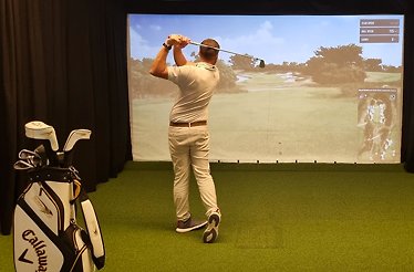 A man playing Golf at Champ du Golf with a screen in front of him.