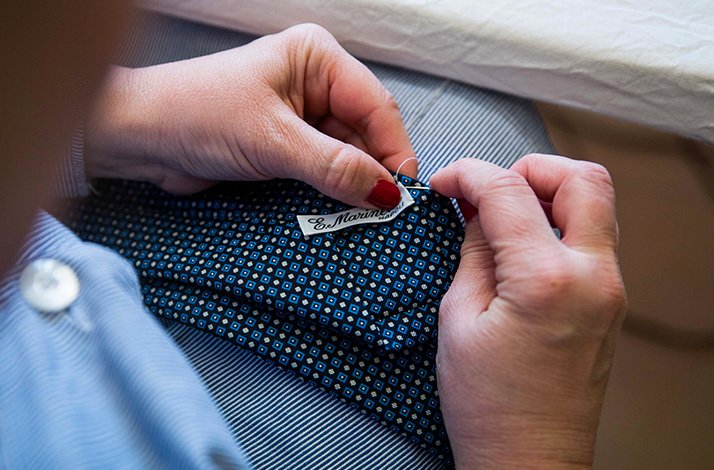 Hands sewing a seamless manual sewing of Eugenio Marinella brand label to a tie.