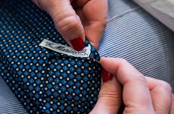 A seamless manual sewing of Eugenio Marinella brand label to a tie.