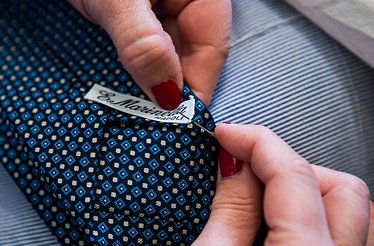 A seamless manual sewing of Eugenio Marinella brand label to a tie.