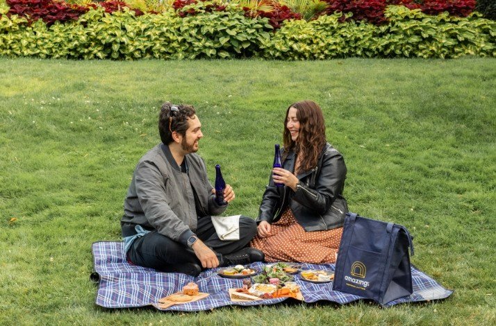 A couple sitting on the grass and having a picnic on a  checkered plaid.