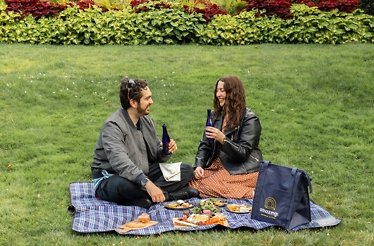 A couple sitting on the grass and having a picnic on a  checkered plaid.