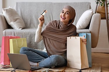 A happy woman with a card in her hands surrounded by purchases from an online store
