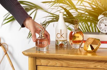 Hand picking up a Jean Paul Gaultier perfume bottle from the dresser top