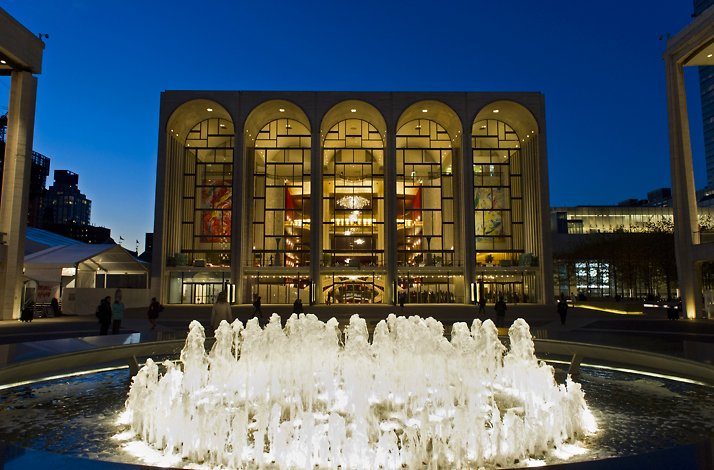 Lincoln Center's Metropolitan Opera House glowing at twilight, featuring five grand arches and a cascading fountain display.