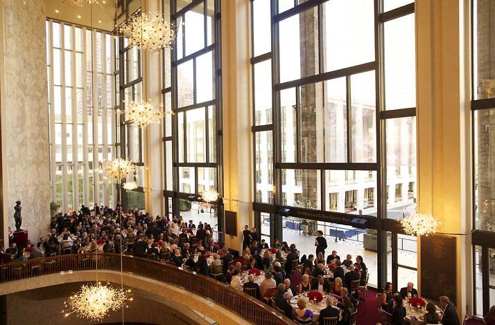 Guests dining at white-tablecloth tables in the Grand Tier lobby beneath glittering chandeliers and floor-to-ceiling windows.