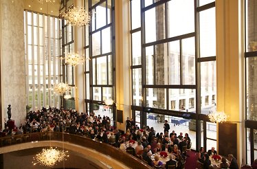 Guests dining at white-tablecloth tables in the Grand Tier lobby beneath glittering chandeliers and floor-to-ceiling windows.