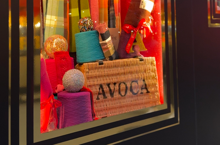 Avoca Suffolk Street Dublin Christmas window display featuring a wicker hamper, colourful yarn spools, glitter baubles, and gift boxes.
