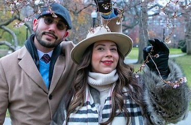 Man wearing brown coat and grey hat and woman in a coat and hat posing for a picture in park during private photo shoot walk in Boston.