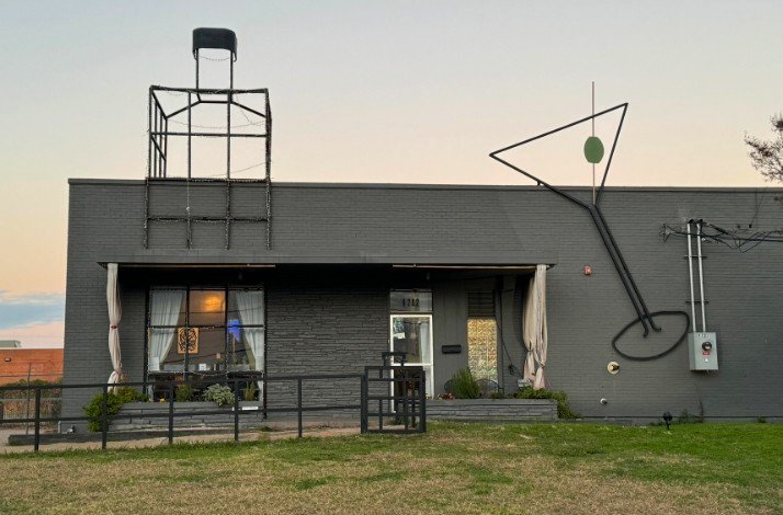 The building of New Artisan Distillery with a bottle and a cocktail glass made of tubes on the roof.