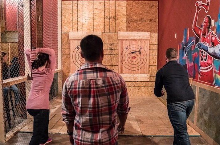 Two participants throwing axes at the targets and the instructor standing between them and watching.