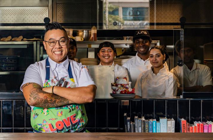 The award-winning Chef Kelvin Cheung is smiling standing in the kitchen with his crew members in the kitchen