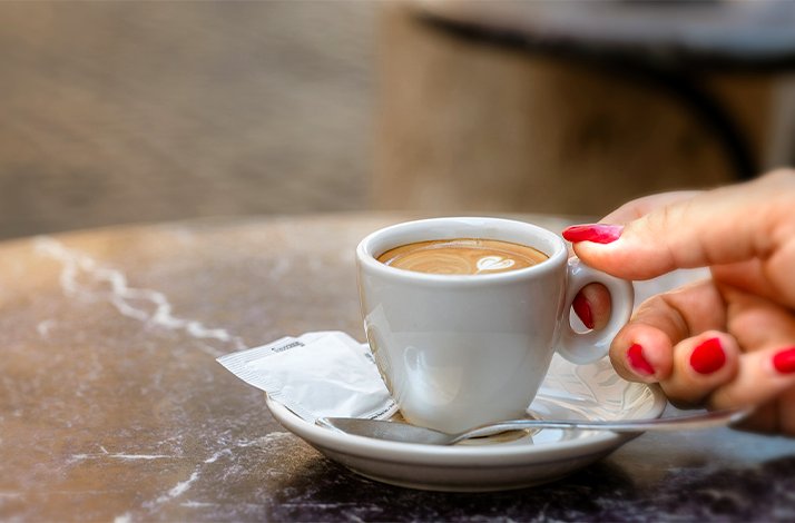 A woman picking up a cup of coffee with her hand.