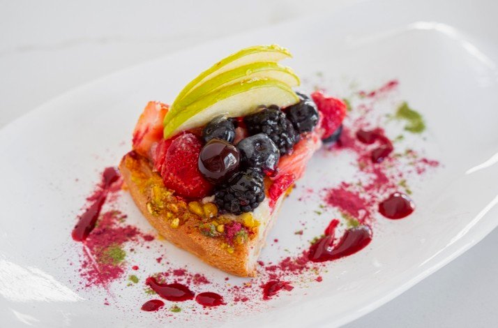 A plate of one portion of cheesecake decorated with berries and sliced apple.