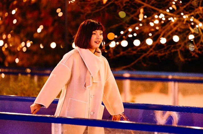 A girl is ice skating at night under festive lights, with Battersea Power Station and a decorated Christmas tree in the background.