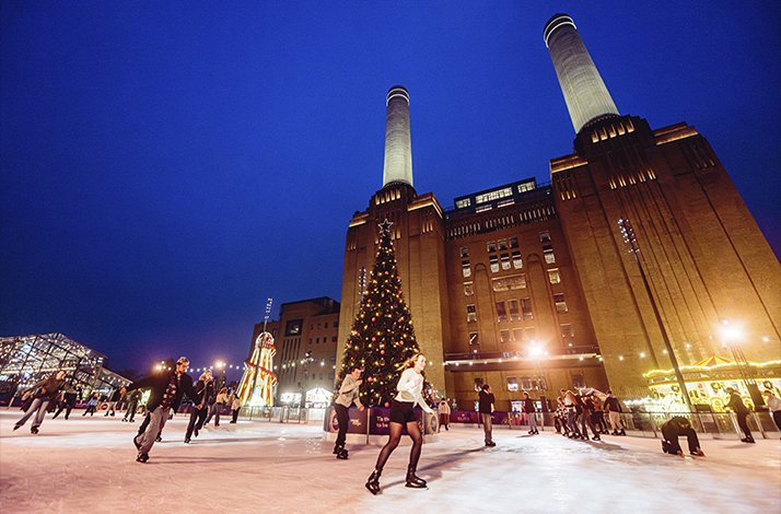 People ice skating at night under festive lights, with Battersea Power Station and a decorated Christmas tree in the background