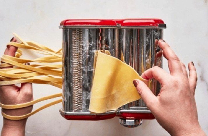 Hands pulling sliced dough out of a pasta maker.