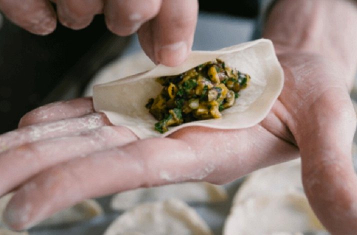 A hand wrapping a dumpling with minced vegetables filling.
