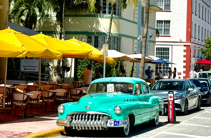 Turquoise vintage car at Everglades market parked next to a cafe with yellow umbrellas.