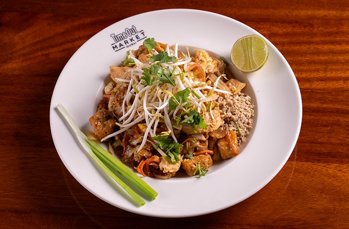 Pad Thai noodles with prawns served in a Time Out Market Dubai plate, topped with bean sprouts, cilantro, crushed peanuts, and lime.