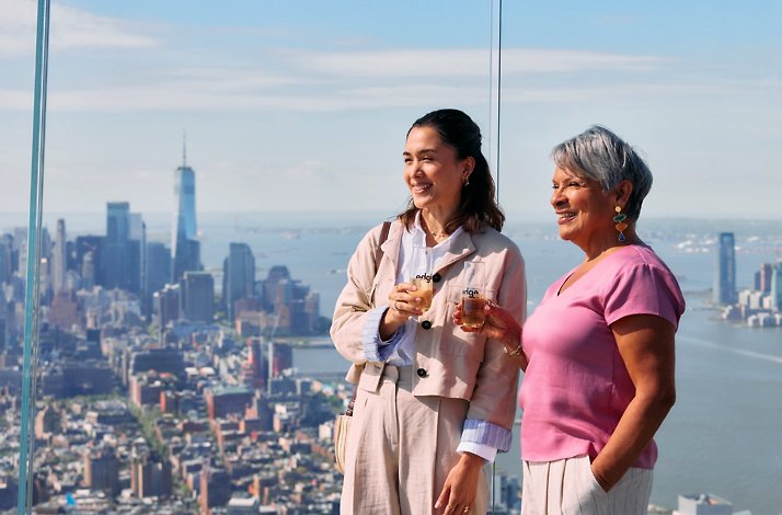 Two woman overlooking the buildings by the glass of the Edge observation deck in New York City.