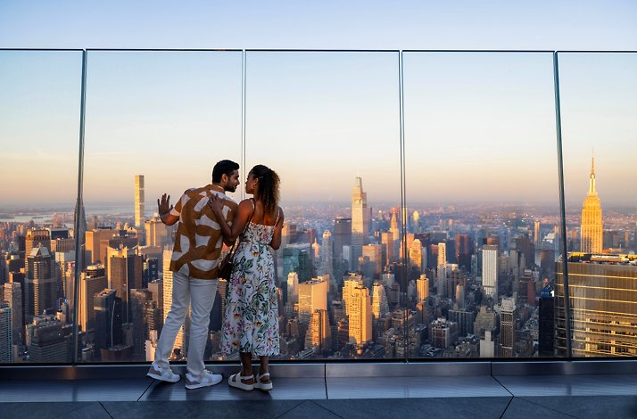 Sip champagne on the highest outdoor sky deck in the Western Hemisphere: In New York, New York The couple are standing at the terrace by the panoramic view of the city.