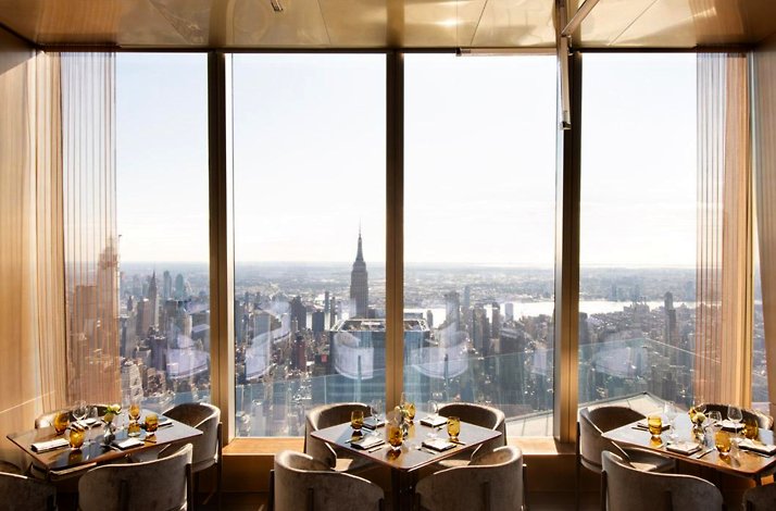 Tables at Peak restaurant on the 101st floor with daytime NYC skyline views.