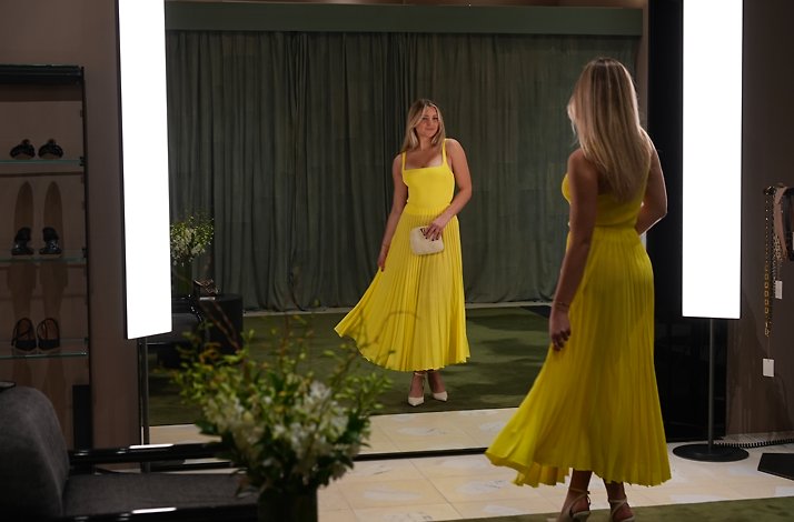 A lady admiring a bright yellow dress in an elegant fitting room with large mirrors.