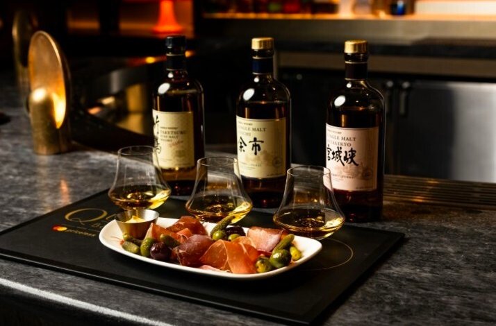 Three bottles and glasses of Japanese whiskey served with a charcuterie plate alongside olives.