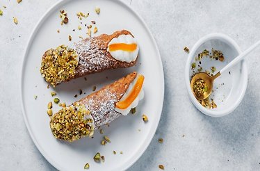 Two Sicilian cannoli topped with pistachios on a white plate.