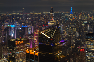 NYC skyline at night with Marquee Sky Deck lit up, city lights and iconic buildings visible.