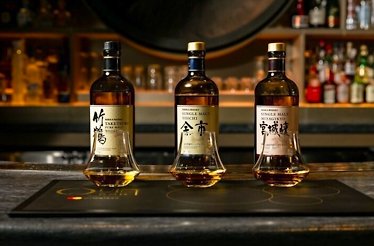 Three bottles of Nikka Japanese whiskey and tasting glasses lined up on a branded Quin Bar placemat.