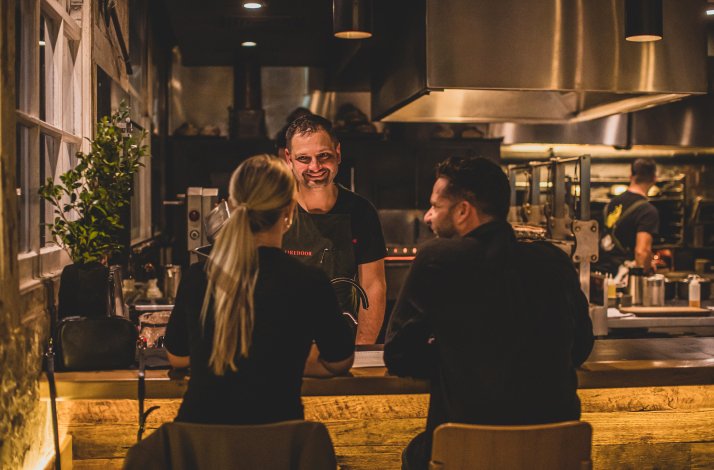 Man and woman chatting with chef Lennox Hastie over the bar stand at Firedoor restaurant in Surry Hills, Australia.
