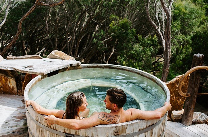 A couple relaxing in a private bath with a beautiful view of nature at the Peninsula Hot Springs resort