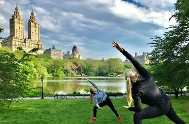 Two women practicing yoga in central park with a view on the San Remo building